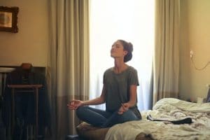 Femme dans une position de méditation sur son lit.